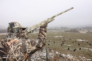 Jäger mit Tarnanzug in Realtree Max-4 ® bei der Krähenjagd am freundlichen Lockbild aus beflockten Lockkrähen